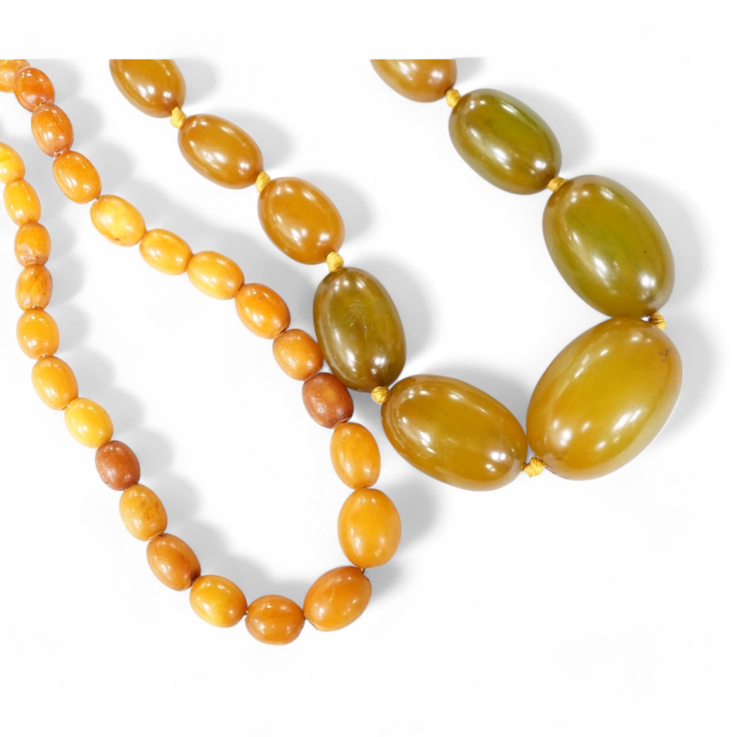 A small single strand graduated oval amber bead necklace, 40cm, gross weight 13 grams, together with a single strand graduated simulated green amber oval bead necklace, 54cm, gross weight 55 grams. Condition - poor to fa